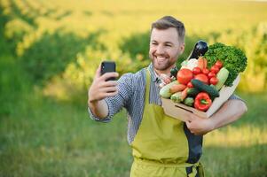 farmer holding a crate of bio vegetables in the farm. Happy man showing box of harvested vegetables. photo