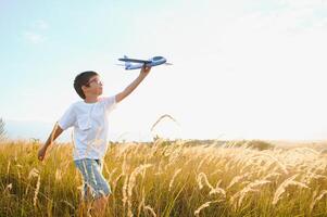 el niño carreras con un juguete avión. hijo Sueños de volador. contento niño, chico, carreras en el Dom jugando con un juguete avión en el verano campo foto