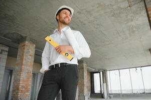 retrato de hombre arquitecto a edificio sitio. confidente construcción gerente vistiendo casco de seguridad. exitoso maduro civil ingeniero a construcción sitio con Copiar espacio. foto