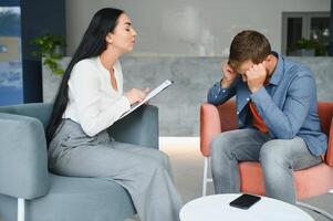 psychology, mental therapy and people concept - woman psychologist talking to sad young man patient at psychotherapy session. photo