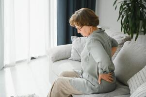 old age, health problem and people concept - senior woman suffering from pain in back or reins at home photo