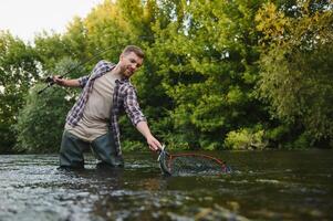 hombre con pescar vara, pescador hombres en río agua exterior. atrapando trucha pescado en neto. verano pescar pasatiempo foto