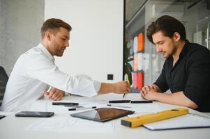 Two engineering working together and using digital tablet looking blueprint and analysis with architectural plan on desk photo