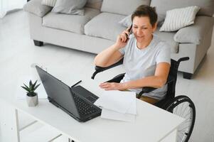 mujer quien usos silla de ruedas trabajando en computadora foto