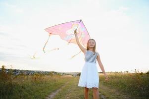 uno contento pequeño niña corriendo en campo con cometa. foto