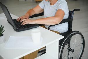persona de libre dedicación en silla de ruedas utilizando ordenador portátil cerca cuaderno y documentos en mesa foto
