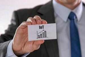 Closeup on businessman holding a card with IoT Internet Of Things rising arrow and chart, business concept photo