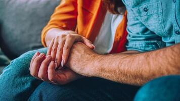 Close up woman and man in love sitting on couch two people holding hands. Symbol sign sincere feelings, compassion, loved one, say sorry. Reliable person, trusted friend, true friendship concept photo