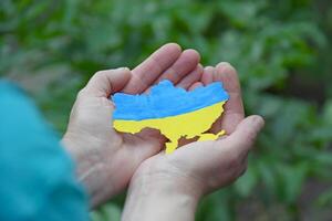 un mujer sostiene en su manos el contorno de el país de Ucrania, decorado me gusta el nacional bandera de Ucrania. foto