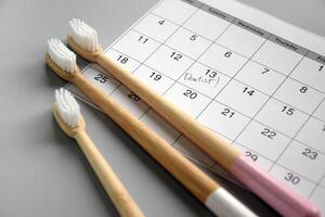 On a light gray background, there is a calendar with a dentist's note and toothbrushes. photo