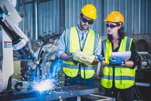 Engineers team mechanic using computer controller Robotic arm for welding steel in steel factory workshop. Industry robot programming software for automated manufacturing technology photo