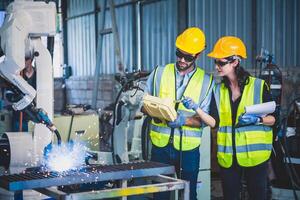 Engineers team mechanic using computer controller Robotic arm for welding steel in steel factory workshop. Industry robot programming software for automated manufacturing technology photo