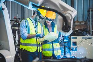 Mecánico del equipo de ingenieros que usa un brazo robótico controlador de computadora para soldar acero en el taller de la fábrica de acero. software de programación de robots industriales para tecnología de fabricación automatizada foto