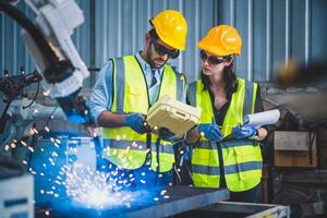 Engineers team mechanic using computer controller Robotic arm for welding steel in steel factory workshop. Industry robot programming software for automated manufacturing technology photo