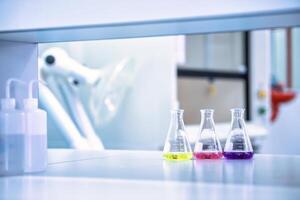 Laboratory flask with colorful liquids stirred inside in laboratory. Science chemistry concept. Blue tone photo