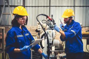 Two engineers mechanic using computer controller Robotic arm for welding steel in steel factory workshop. Industry robot programming software for automated manufacturing technology photo