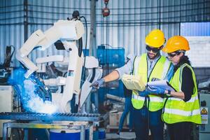 Mecánico del equipo de ingenieros que usa un brazo robótico controlador de computadora para soldar acero en el taller de la fábrica de acero. software de programación de robots industriales para tecnología de fabricación automatizada foto