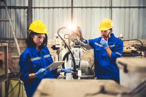 Two engineers mechanic using computer controller Robotic arm for welding steel in steel factory workshop. Industry robot programming software for automated manufacturing technology . photo