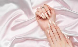 Female Hands on a white silk background with beautiful pearl manicure photo