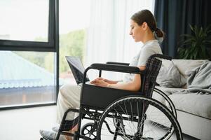 Female freelance programmer sitting in wheelchair and using computers while coding web game at home. photo