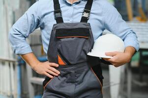 Portrait of factory worker in protective uniform and hardhat standing by industrial machine at production line. People working in industry photo