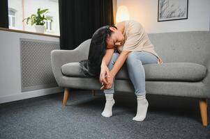 Upset woman frustrated by problem with work or relationships, sitting on couch, embracing knees, covered face in hand, feeling despair and anxiety, loneliness, having psychological trouble. photo