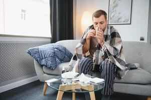 A sick man sits at home on a gray sofa with a blanket. Illness, protection, coronavirus, illness, flu photo