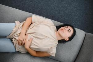 joven mujer sufrimiento desde abdominal dolor a hogar. ginecología concepto foto