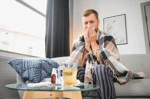 Sick man on sofa at home and blowing nose photo