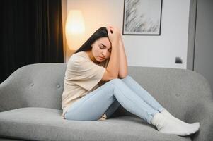 Upset woman frustrated by problem with work or relationships, sitting on couch, embracing knees, covered face in hand, feeling despair and anxiety, loneliness, having psychological trouble. photo
