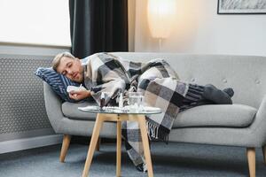 A sick man sits at home on a gray sofa with a blanket. Illness, protection, coronavirus, illness, flu photo