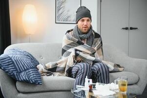 A sick man sits at home on a gray sofa with a blanket. Illness, protection, coronavirus, illness, flu photo