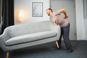 joven hombre sufrimiento desde espalda dolor después que lleva pesado mueble. foto