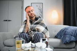 Young man suffering from cold at his home. Shot of a young man sitting on his bed while feeling unwell at home. Trying to stay warm. Sick man photo