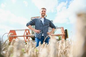 Handsome farmer with tablet standing in front of combine harvester during harvest in field. photo