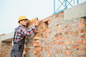 Using bricks. Young construction worker in uniform is busy at the unfinished building photo