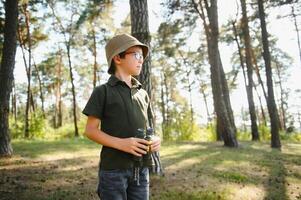 pequeño chico explorar con prismáticos durante excursionismo en otoño bosque. conceptos de aventura, exploración y excursionismo turismo para niños. foto