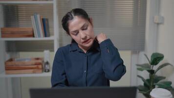 mulher sente cansado, tem pescoço dor enquanto trabalhando usando uma computador portátil enquanto sentado às trabalhar, sobrecarregado fêmea empregado video