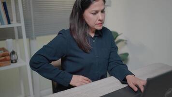 mujer mira a cuaderno pantalla con tristeza y temor y siente estómago dolor mientras trabajando en ordenador portátil video