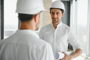 A front view of two smart architects with white helmets reviewing blueprints at a construction site on a bright sunny day photo