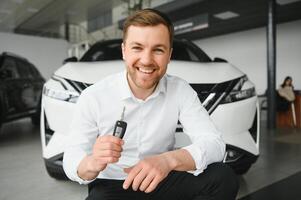 Happy buyer holding keys near the car in front of the modern avtosalon building photo