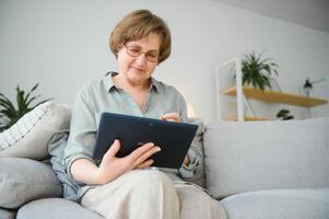 Senior woman looking and laughing at her digital tablet on sofa photo