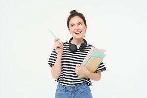 Portrait of young woman, student with notebooks and earphones on her neck, posing for college advertisement, white background photo