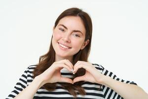 retrato de sonriente, contento Novia muestra corazón con manos y mirando con cuidado a cámara, Rápido su amor o afecto, me gusta producto, en pie terminado blanco estudio antecedentes foto