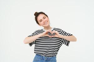 Beautiful european woman, shows heart sign, expresses her love and affection, flirting, standing over white background photo