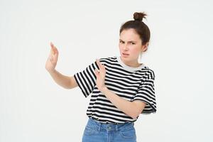 Image of woman expressing aversion, dislike something, looks apalled, extends hands forward in defensive gesture, rejecting, refusing, standing over white background photo