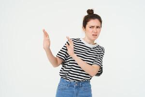 Image of woman expressing aversion, dislike something, looks apalled, extends hands forward in defensive gesture, rejecting, refusing, standing over white background photo