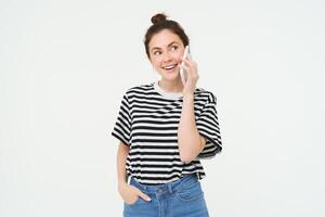 Happy young woman talks on mobile phone, chats on telephone, uses smartphone, stands over white background photo