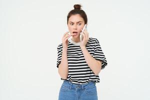 Image of woman with shocked face, looks confused while chats over the phone, listens to person on telephone, white background photo