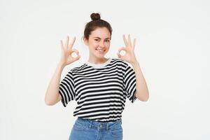 excelente elección. sonriente elegante joven mujer, demostración bueno, Okay gesto, cero firmar, en pie terminado blanco antecedentes foto